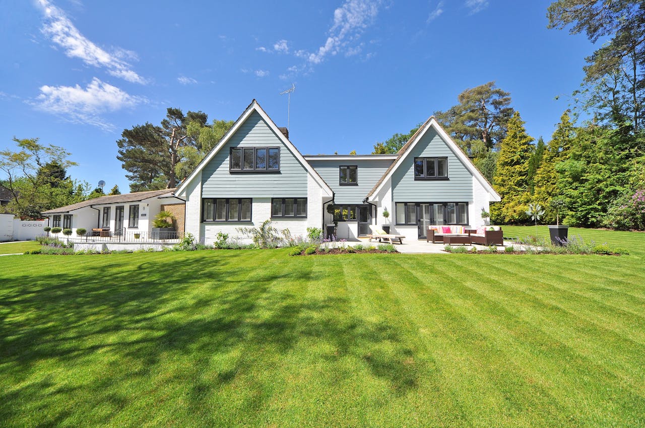 Modern family home exterior showcasing a large lawn and garden under a clear blue sky.